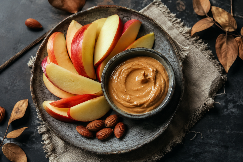 Slices of fresh red apples served on a rustic plate with a small bowl of creamy almond butter and whole almonds.