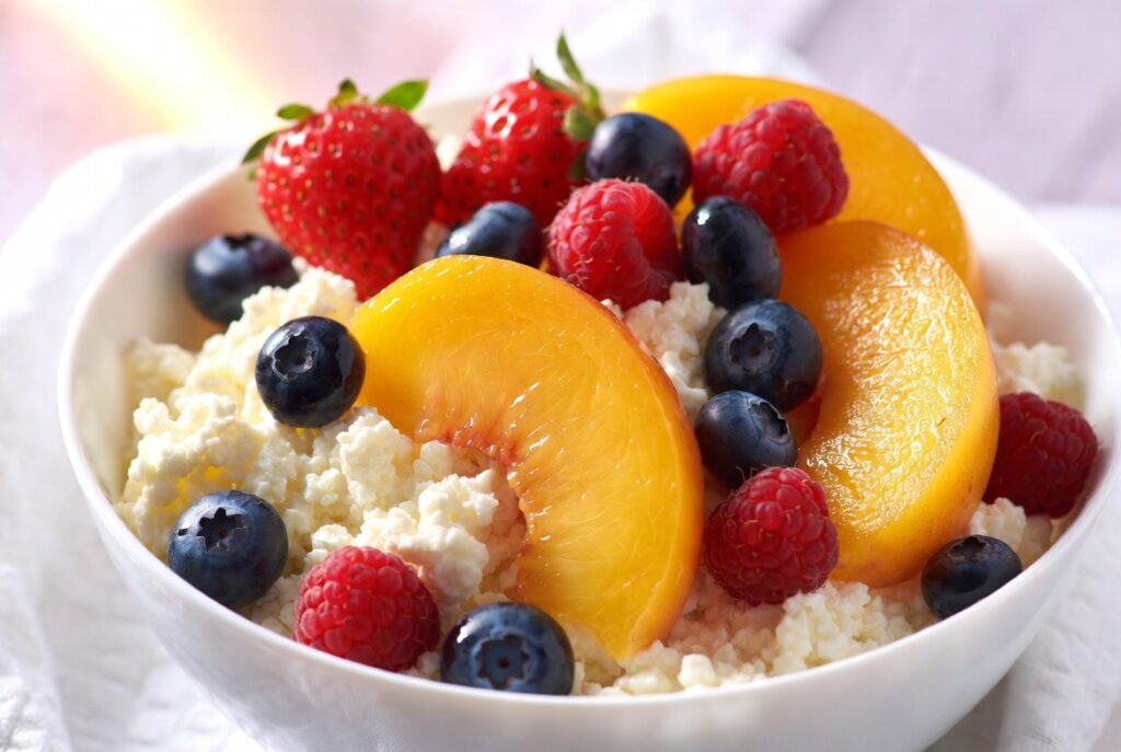 Creamy cottage cheese topped with sliced peaches and fresh berries in a ceramic bowl, soft appetizing food photography