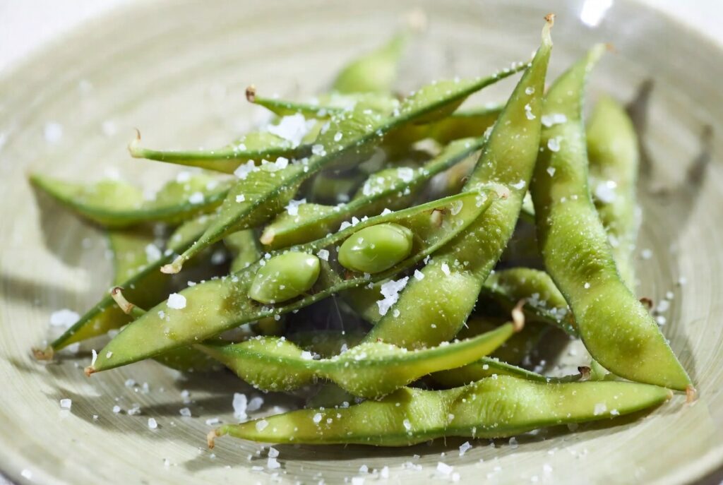 Fresh green edamame pods sprinkled with coarse sea salt on a minimalist plate, vibrant healthy snack photography