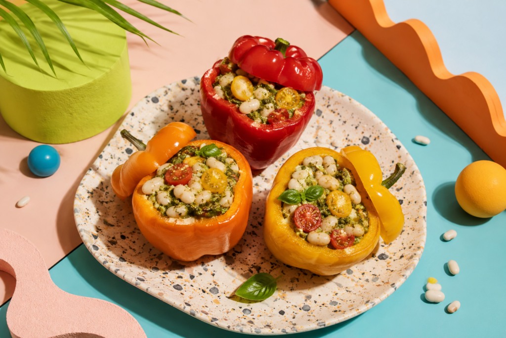 Three colorful pesto white bean stuffed bell peppers served on a spotted plate with fun summer vibes and fiber-rich summer recipes inspiration